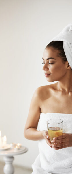 Beautiful african girl with towel on head holding glass smiling looking in side resting in spa resort. Copy space.